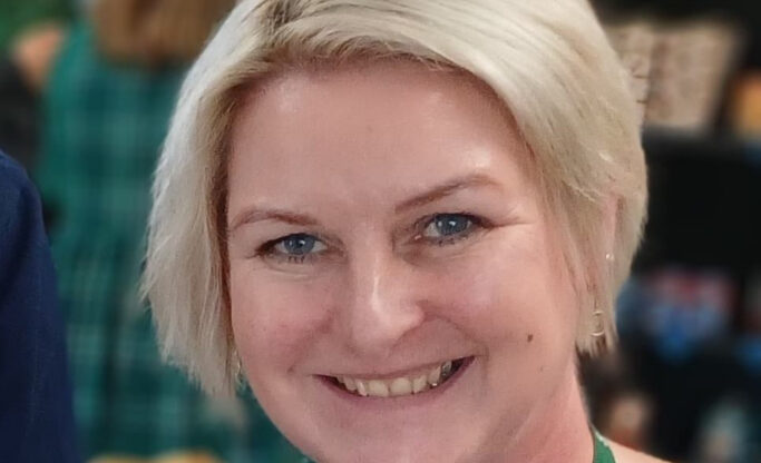 Portrait of director Zoe who has a blonde bob and is wearing a blue top